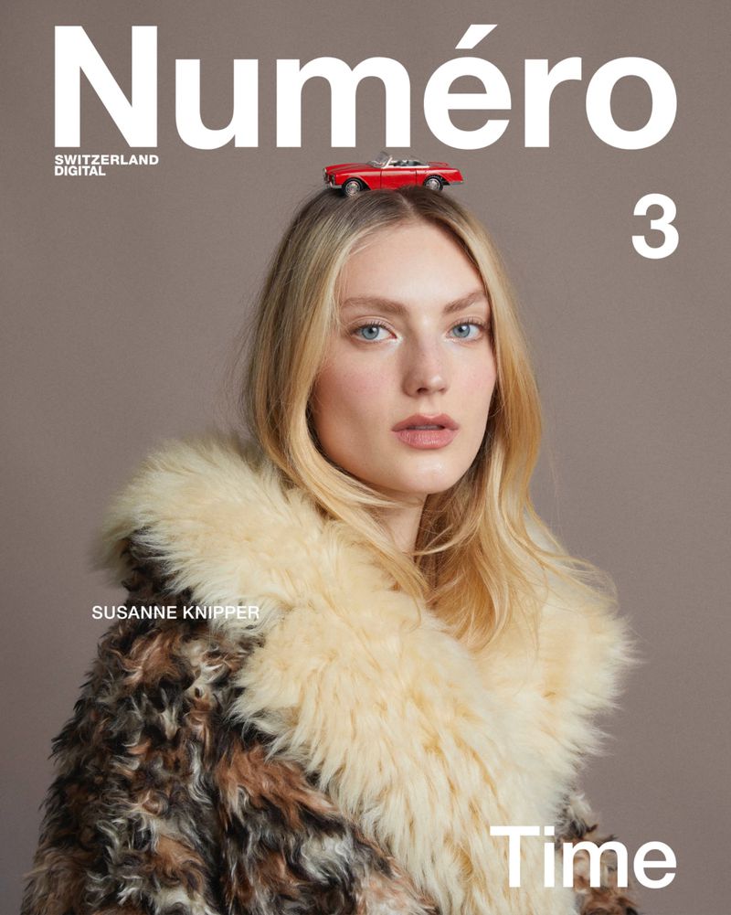 Magazine cover featuring a fair-skinned woman with blonde hair, wearing a fur coat, topped with a red toy car against a neutral background.