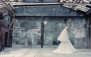 Model in a voluminous white tulle gown posing inside an expansive industrial warehouse with weathered concrete walls.