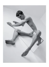 Monochrome studio portrait of a young man posed with a rectangular mirror intersecting his body on white seamless background.