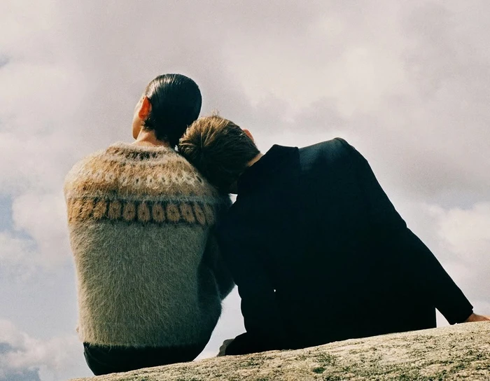 Two people viewed from behind seated closely against an outdoor sky background