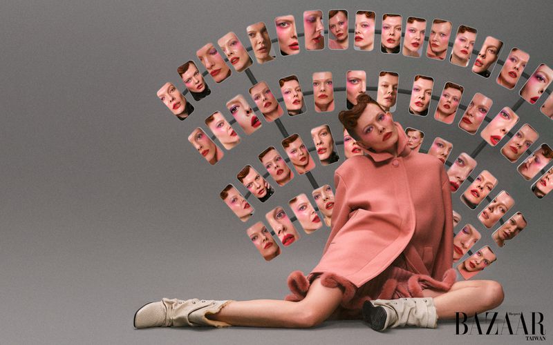 Conceptual fashion shot features a woman in a pink coat surrounded by multiple headshot portraits, posing against a grey backdrop.