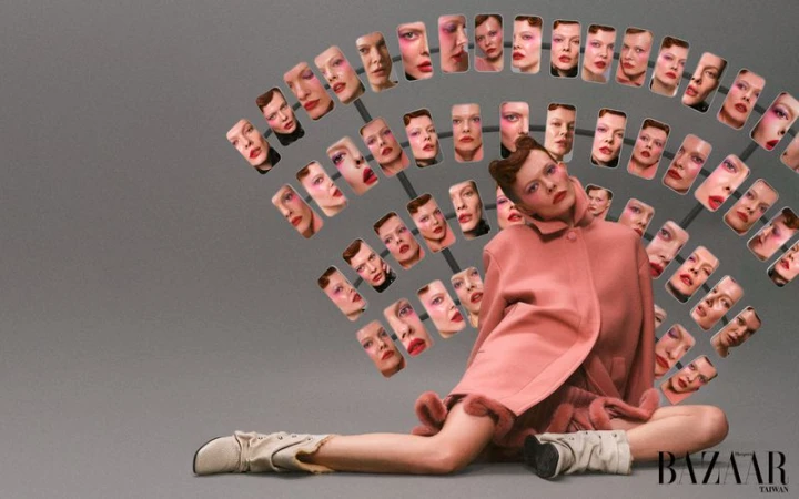 Conceptual fashion shot features a woman in a pink coat surrounded by multiple headshot portraits, posing against a grey backdrop.