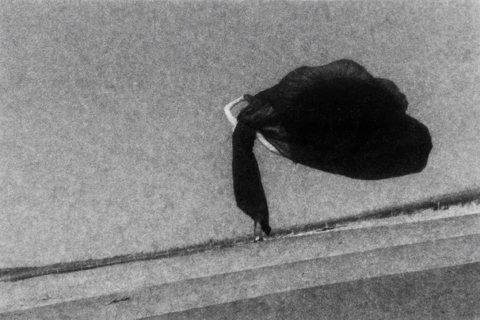 Black and white fine art photograph of a dark object, possibly a bag, placed on concrete steps in an outdoor setting under natural light.