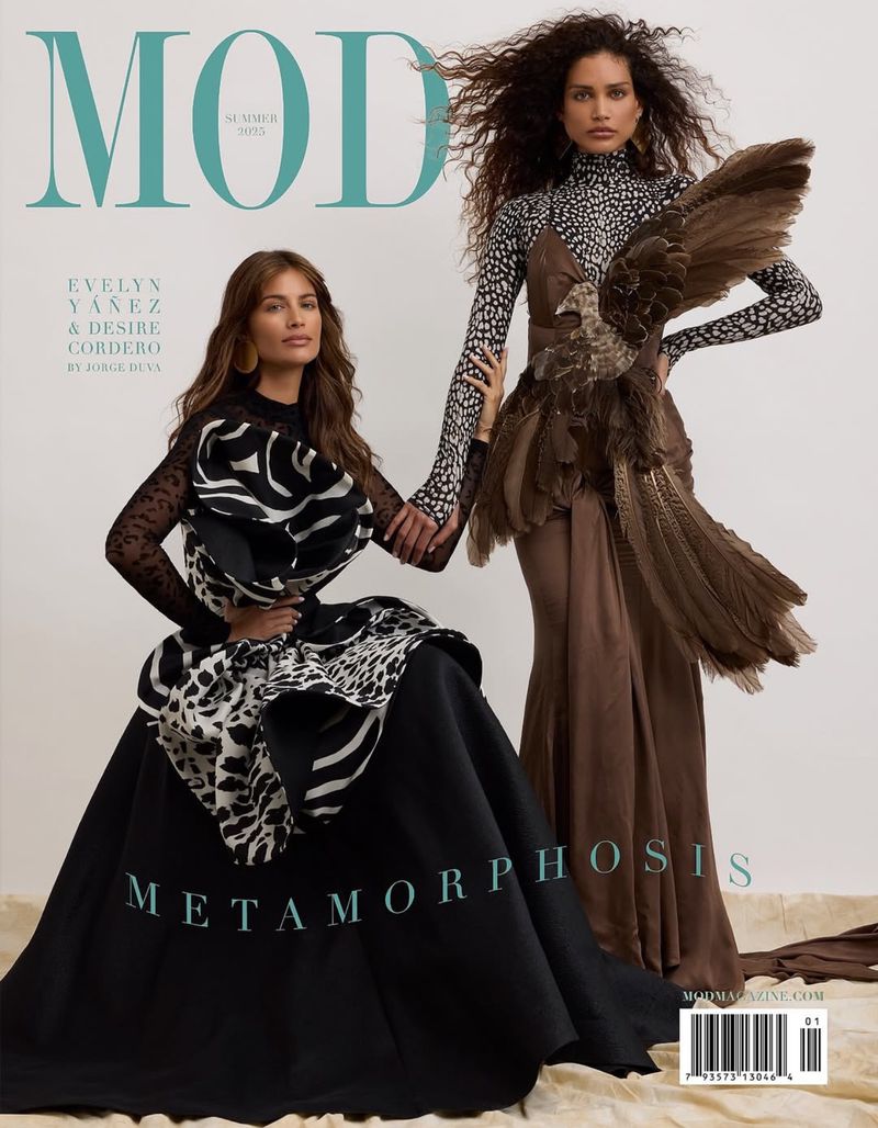 Two fashion models pose on a magazine cover, one seated in a black gown, the other standing in a brown gown with feathers. 