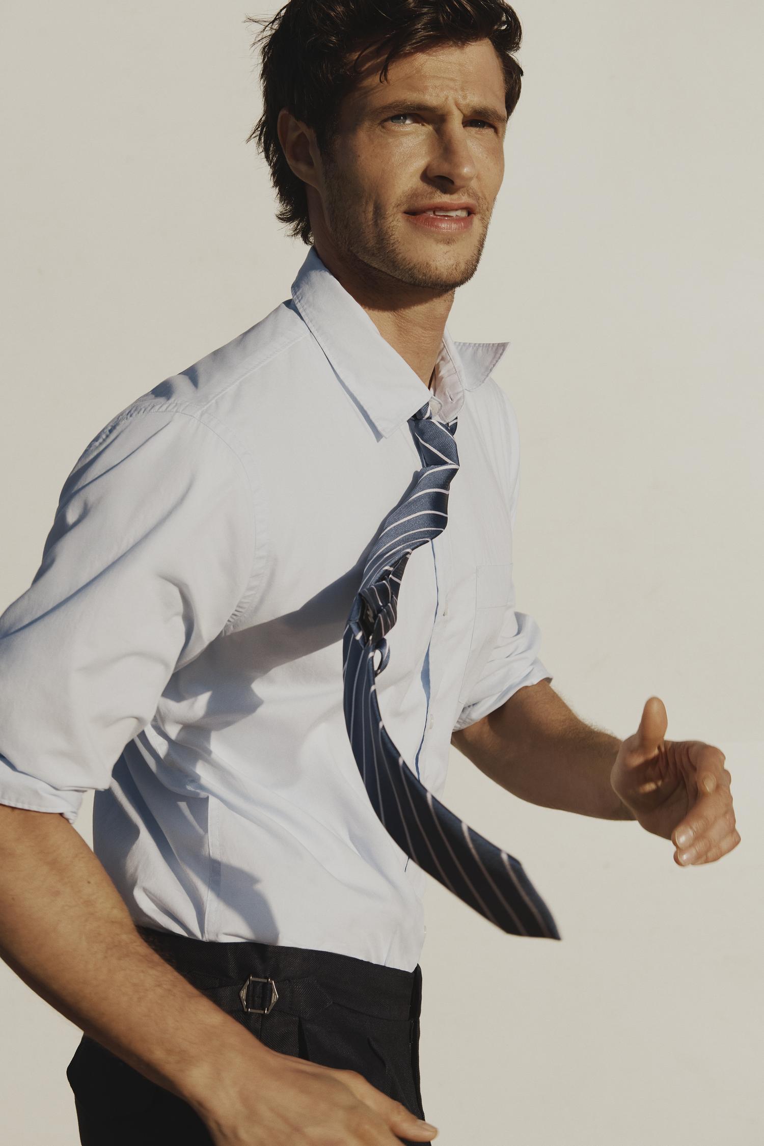 Handsome man in an unbuttoned shirt with a tie in motion, against a clean background, capturing a blend of fashion and natural light.
