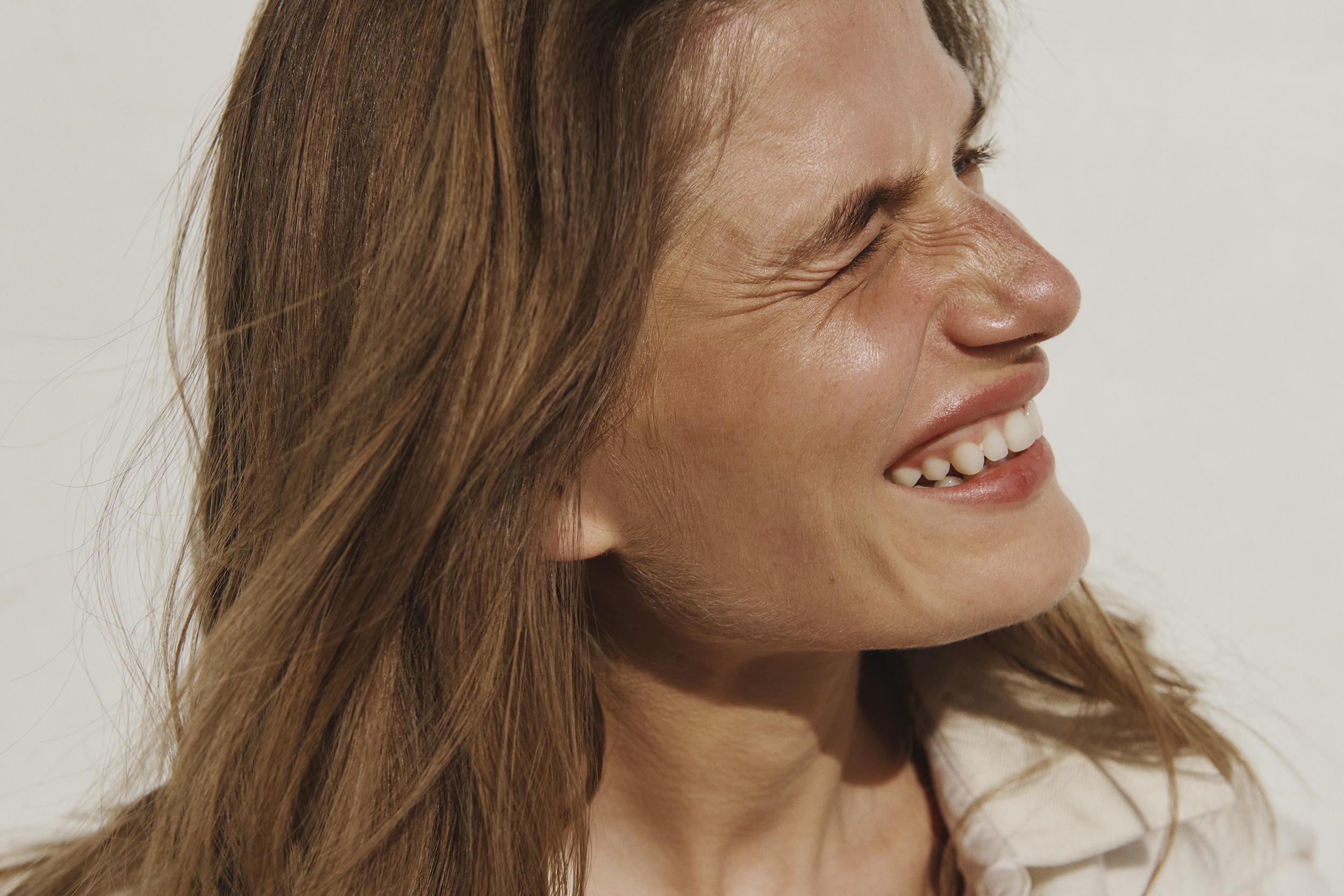 Close-up studio portrait of a smiling adult woman with medium brown hair, wearing a collared shirt against a white backdrop.