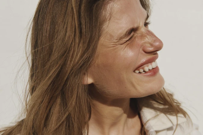 Close-up studio portrait of a smiling adult woman with medium brown hair, wearing a collared shirt against a white backdrop.