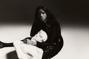 Model Onyinyechi Chijioke seated in dark apparel cradling a white classical plaster bust in a studio setting.