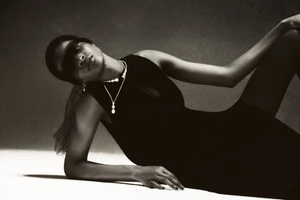 Model in black dress with layered necklaces reclining on a studio surface in a monochrome fashion portrait for Numero Switzerland