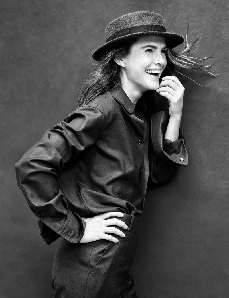 Black and white portrait of Keri Russell laughing in profile wearing a dark button-up shirt and a felt hat with ribbon trim.