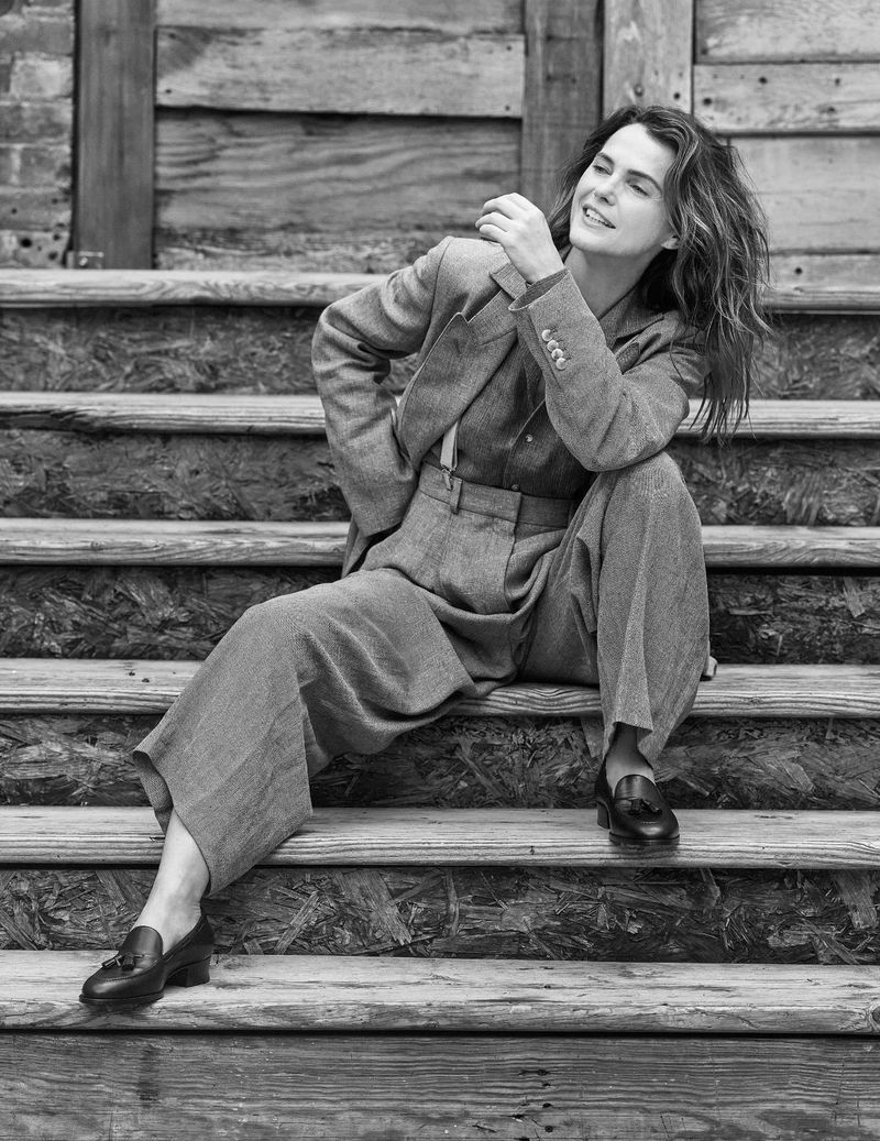 Black and white portrait of an adult woman in a business suit, seated on wooden steps, looking up, showcasing a blend of style and serenity.