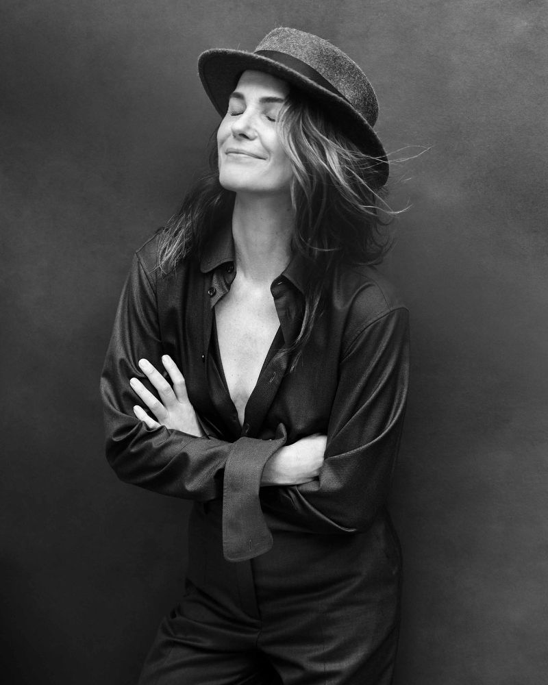Black and white portrait of Keri Russell wearing a fedora hat and dark unbuttoned shirt with arms crossed and eyes closed.