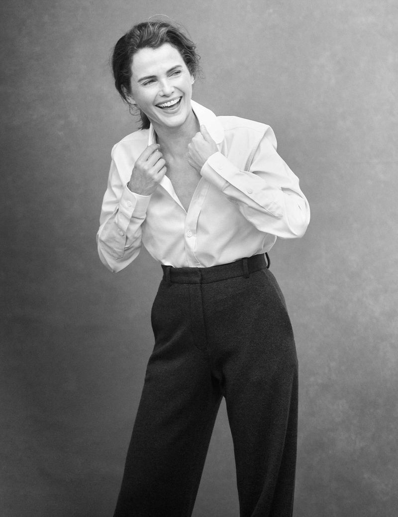 Black and white portrait of an adult woman with a happy facial expression, wearing a button-down shirt and trousers in a photo studio setting.