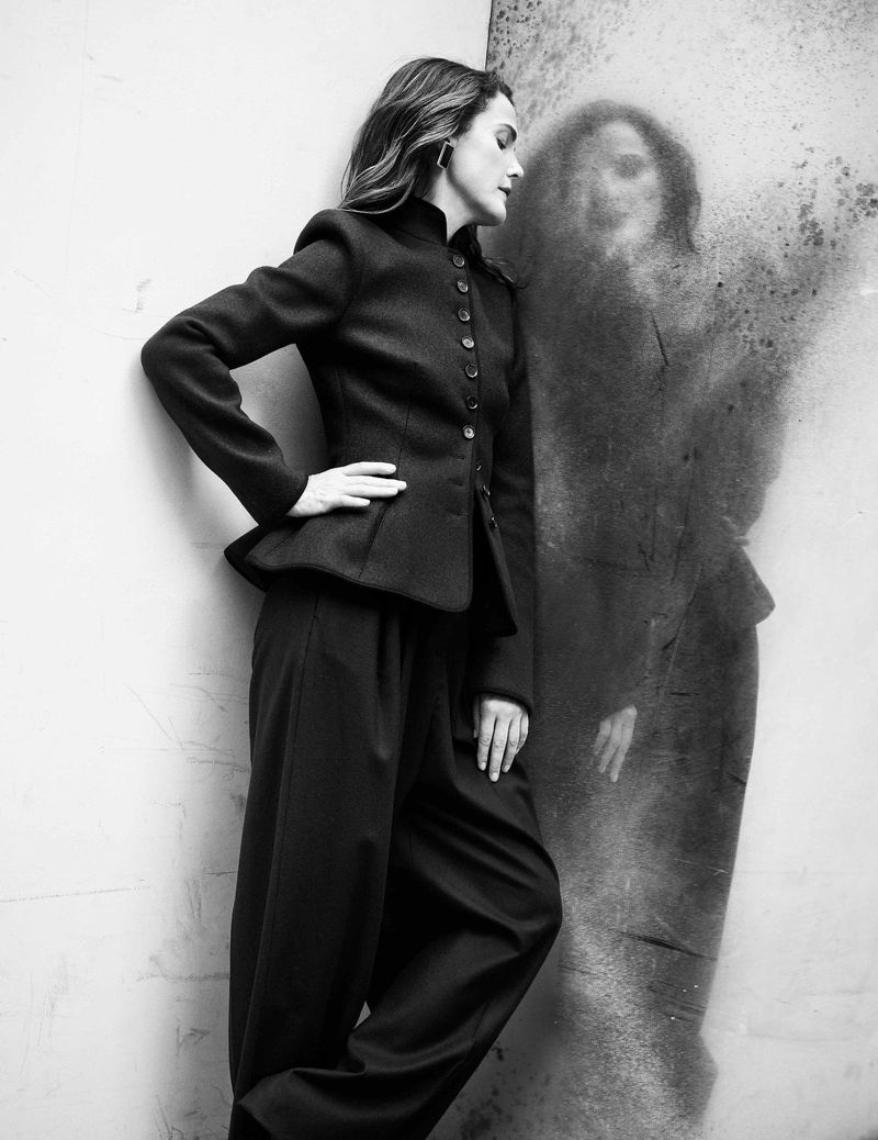 Monochrome fashion shot of woman in blazer and wide-legged pants, posing against textured wall with ghost-like image reflected.