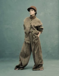 Keri Russell posing barefoot in an oversized brown tweed suit and brown hat against a mottled teal backdrop.