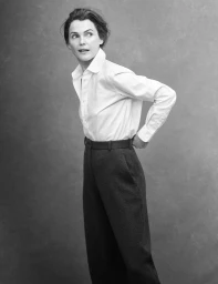 Keri Russell in a white button-down shirt and dark high-waisted trousers posing against a textured grey studio backdrop.