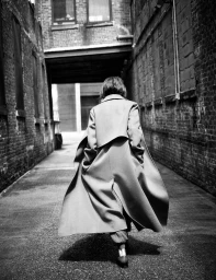 Keri Russell seen from behind walking down an urban brick alley wearing a flowing long coat in black and white.