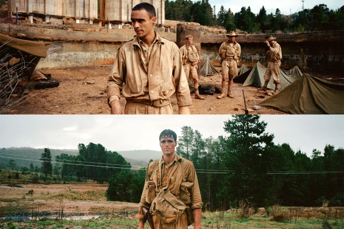 Men in vintage military uniforms stand outdoors near tents and construction, depicting a historical or war-related scene with natural light.