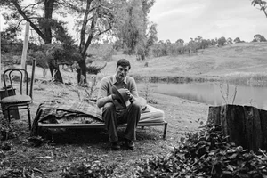Jacob Elordi seated on an outdoor cot holding a hat in a rural landscape for Vogue Australia photographed by Isabella Elordi