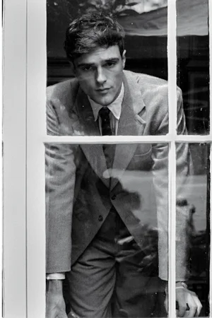 Jacob Elordi wearing a suit and tie looking through a multi-pane window in a black and white editorial portrait.