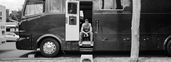 Monochrome image of actor Jacob Elordi sitting shirtless in the open doorway of a large motorhome for Vogue Australia.