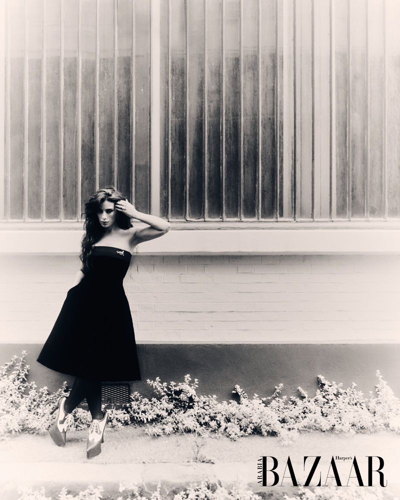 Black and white fashion shot of a brunette adult female model in a strapless black dress posing in front of a frosted window.