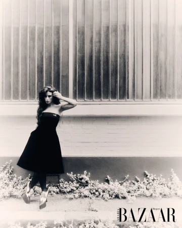 Black and white fashion shot of a brunette adult female model in a strapless black dress posing in front of a frosted window.