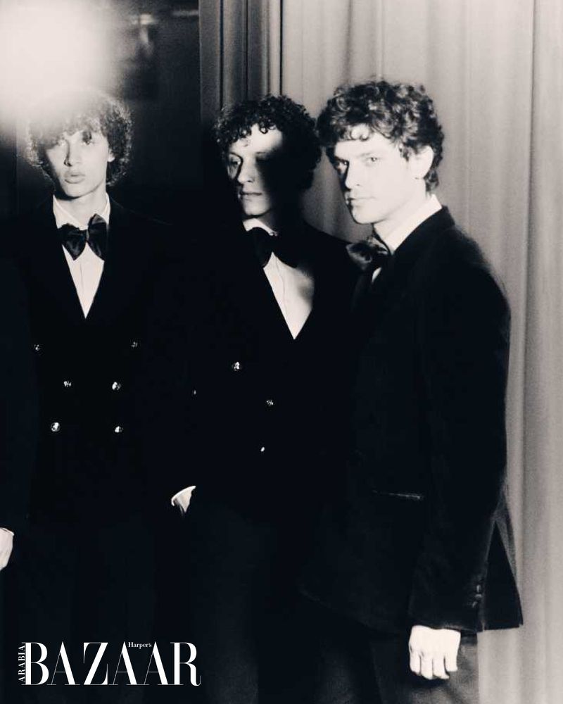 Three male fashion models pose in black suits and bow ties against a neutral backdrop for Harper's Bazaar magazine cover.