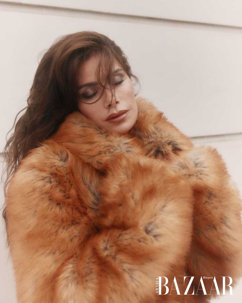 Brunette woman in faux fur coat with eyes closed, shot indoors. Fashion editorial with elegant and soft lighting.