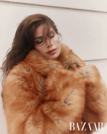 Brunette woman in faux fur coat with eyes closed, shot indoors. Fashion editorial with elegant and soft lighting.