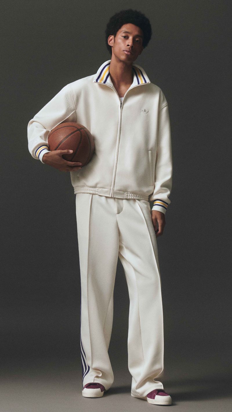 A young adult man in a cream-colored tracksuit holding a basketball in a studio setting, showcasing a blend of athletic wear and lifestyle fashion.