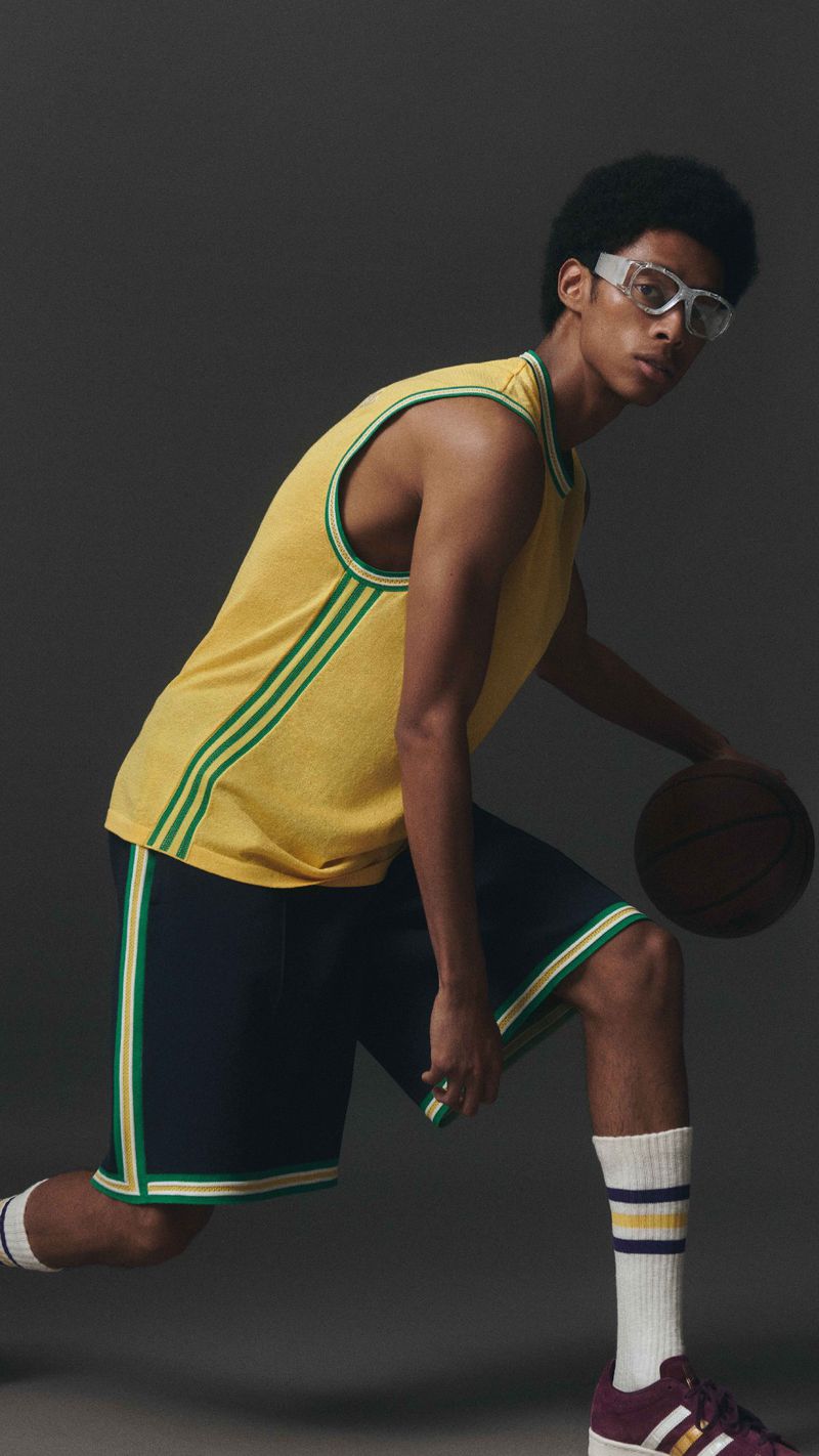 Man in yellow jersey and blue shorts dribbles a basketball in a studio setting, showcasing an athletic and stylish pose.