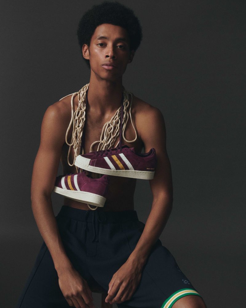 Dark-haired person sits and holds a pair of burgundy and yellow sneakers. The sneakers hang from a rope around the neck.