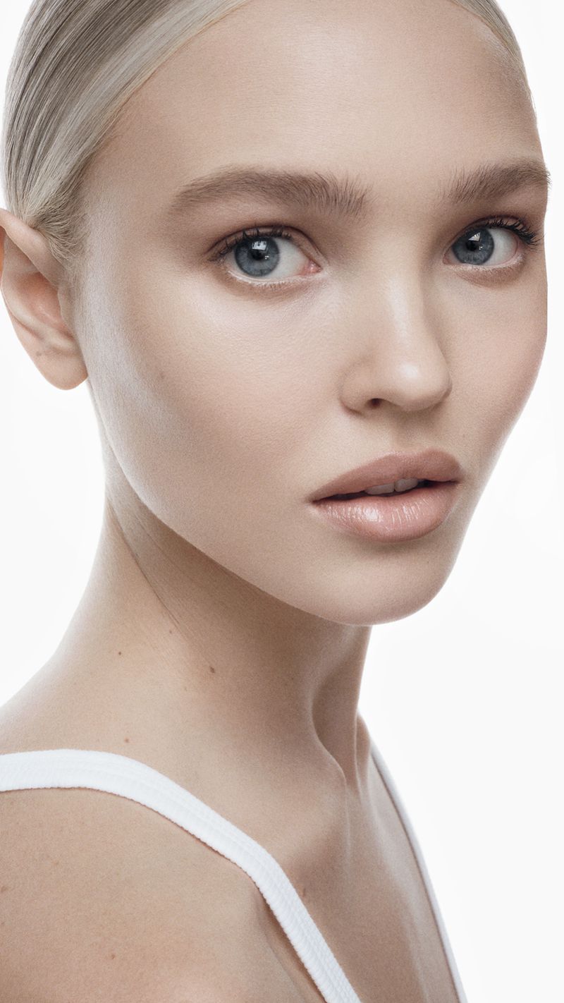Close-up portrait of a blonde woman with blue eyes and fair skin, posing in front of a bright white background. Beauty and fashion.