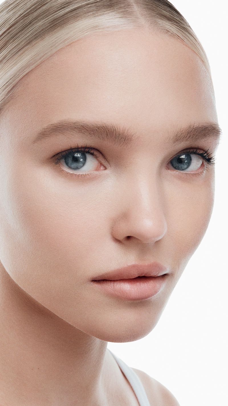 Close-up portrait of a young fair-skinned blonde woman with blue eyes against a white background in a beauty shot.