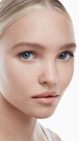 Close-up beauty portrait of model Thea Ros with natural dewy makeup and blonde hair against a bright white background.