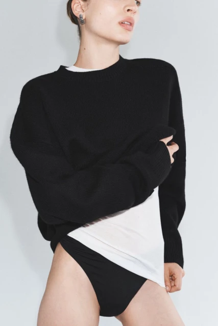 Portrait of a young woman in a black sweater and black underwear against a neutral background, showcasing modern fashion.