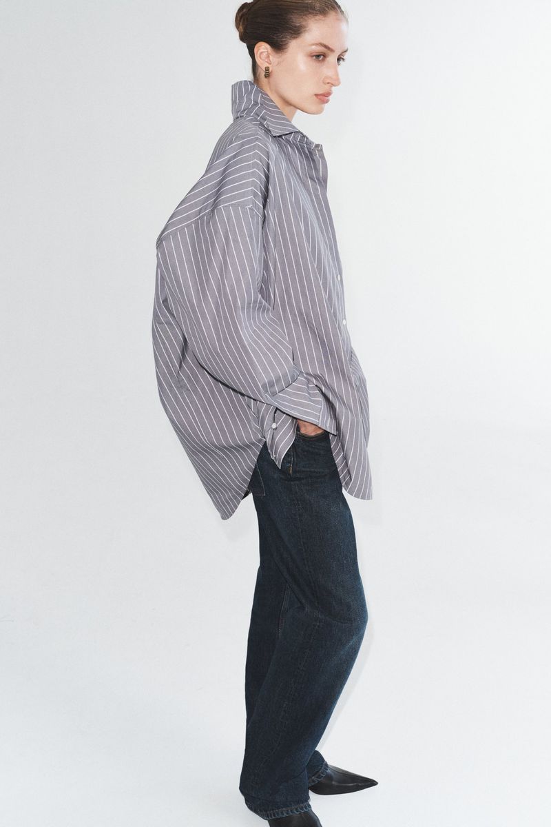 Woman in a striped shirt and blue jeans posing in a white studio. Fashion editorial photograph of a stylish outfit.