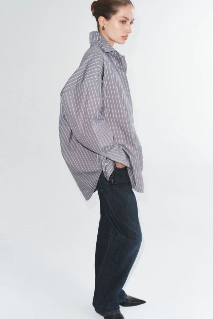 Woman in a striped shirt and blue jeans posing in a white studio. Fashion editorial photograph of a stylish outfit.