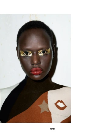 Fashion portrait of a woman with gold eye makeup, red lipstick, and patterned top against a muted white background. Studio lighting.