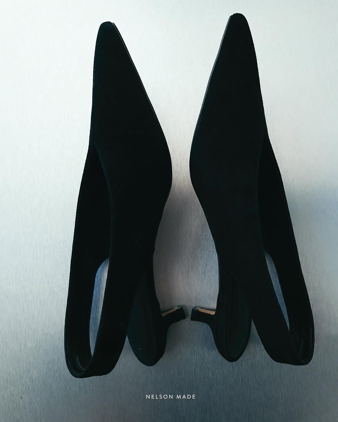 A pair of black pointed-toe slingback heels are displayed on a metallic surface, showcasing their sleek design and elegant silhouette.