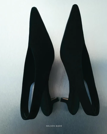 A pair of black pointed-toe slingback heels are displayed on a metallic surface, showcasing their sleek design and elegant silhouette.