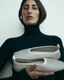 Model holding cream mesh flats wearing a black turtleneck against a white background for Nelson Made FW25 campaign.