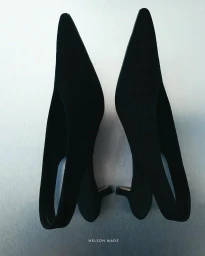 Two black pointed-toe slingback heels placed upright against a light grey gradient background.