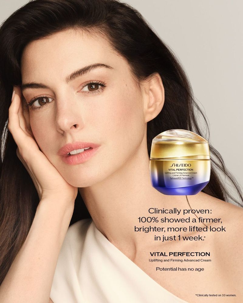 Close-up beauty shot of a woman with dark hair, fair skin, and light-colored top, alongside a jar of Shiseido Vital Perfection cream.