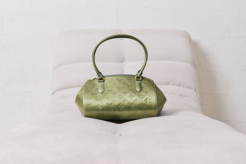 Olive green Louis Vuitton handbag on soft white surface. The handbag has an embossed pattern, rounded handle, and a slight sheen.