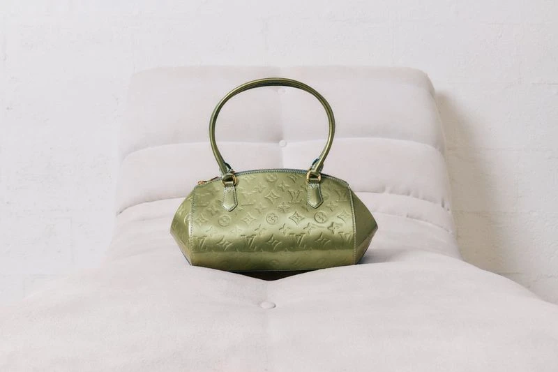 Olive green Louis Vuitton handbag on soft white surface. The handbag has an embossed pattern, rounded handle, and a slight sheen.