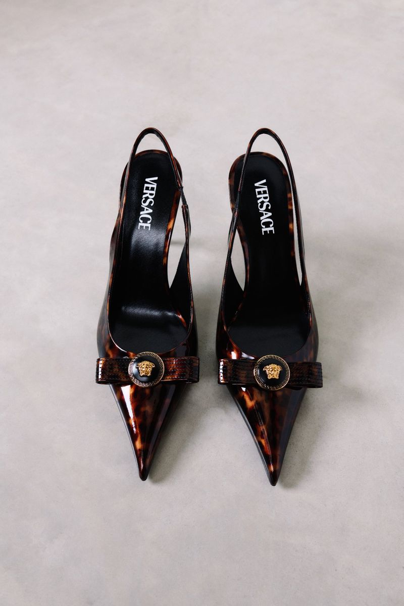 Versace slingback pumps with a pointed toe and tortoiseshell pattern, adorned with a round Medusa emblem, displayed on a gray surface.