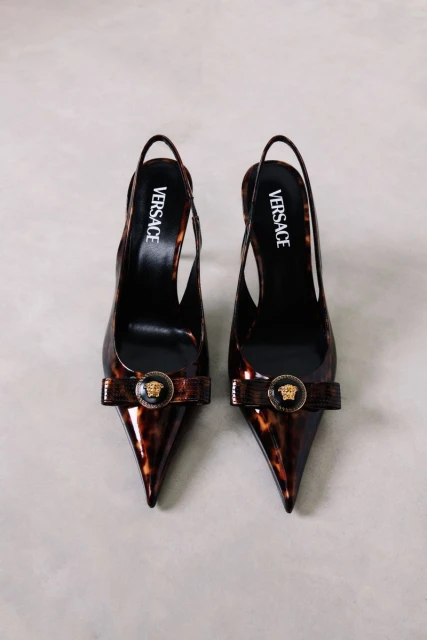 Versace slingback pumps with a pointed toe and tortoiseshell pattern, adorned with a round Medusa emblem, displayed on a gray surface.