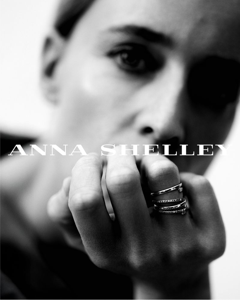 Monochrome close-up of a woman's face and hand wearing multiple rings, showcasing beauty and fashion jewelry in a clean, bright setting.
